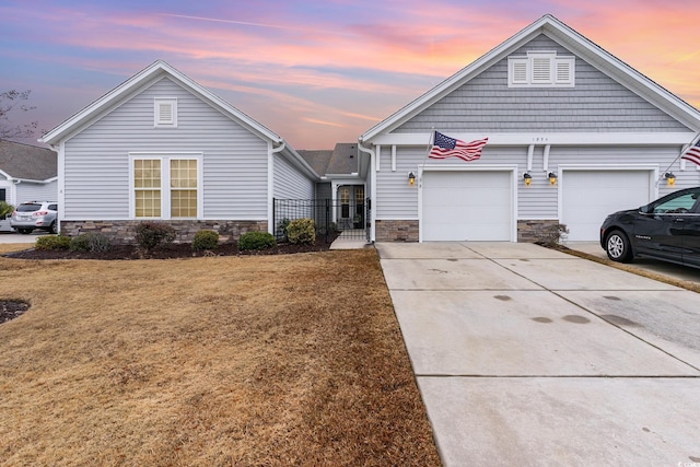 view of front facade with a yard, stone siding, an attached garage, and driveway