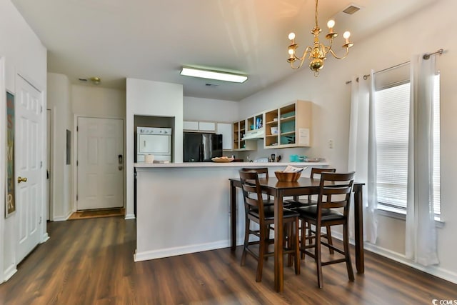 dining space with stacked washer and dryer, dark hardwood / wood-style floors, and a chandelier