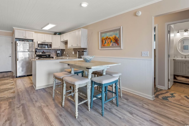 kitchen with appliances with stainless steel finishes, white cabinets, kitchen peninsula, crown molding, and light wood-type flooring