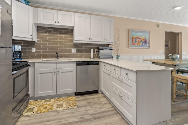 kitchen with sink, crown molding, white cabinetry, stainless steel appliances, and kitchen peninsula