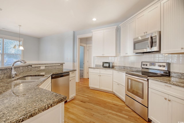 kitchen with stainless steel appliances, a sink, white cabinetry, hanging light fixtures, and light wood finished floors