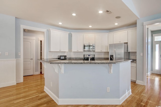 kitchen with stainless steel appliances, light wood-type flooring, visible vents, and a breakfast bar area