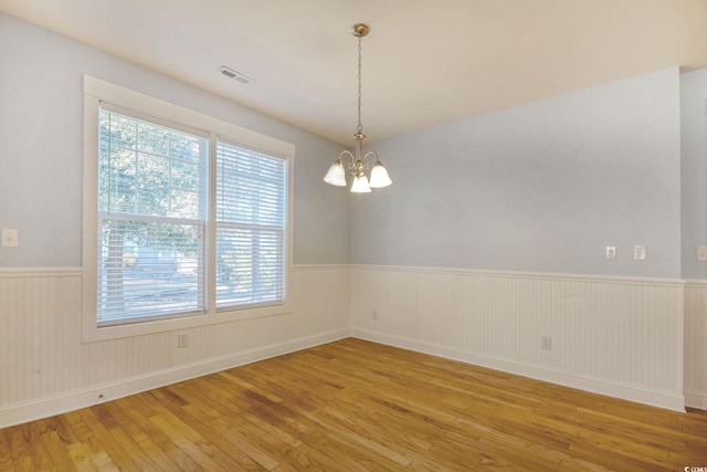 empty room featuring visible vents, wainscoting, hardwood / wood-style flooring, and an inviting chandelier