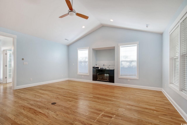 unfurnished living room featuring light wood-style floors, a glass covered fireplace, vaulted ceiling, and baseboards