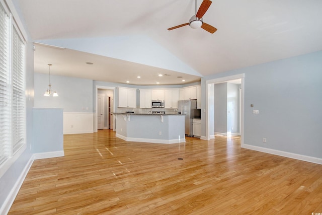 unfurnished living room with recessed lighting, high vaulted ceiling, light wood-type flooring, baseboards, and ceiling fan with notable chandelier