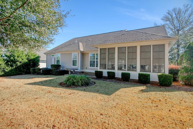 rear view of house with a sunroom, roof with shingles, and a lawn