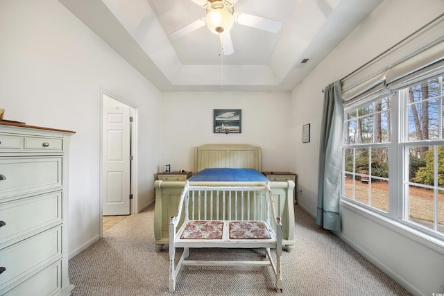 carpeted bedroom with ceiling fan, a tray ceiling, and multiple windows