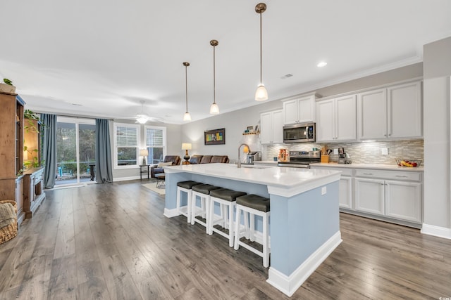 kitchen with a breakfast bar area, white cabinetry, a kitchen island with sink, stainless steel appliances, and decorative light fixtures