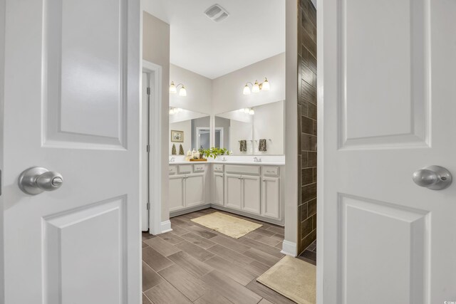 full bath with double vanity, visible vents, wood finish floors, and tiled shower