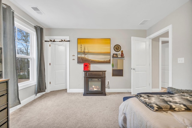 carpeted bedroom featuring a glass covered fireplace, visible vents, and baseboards
