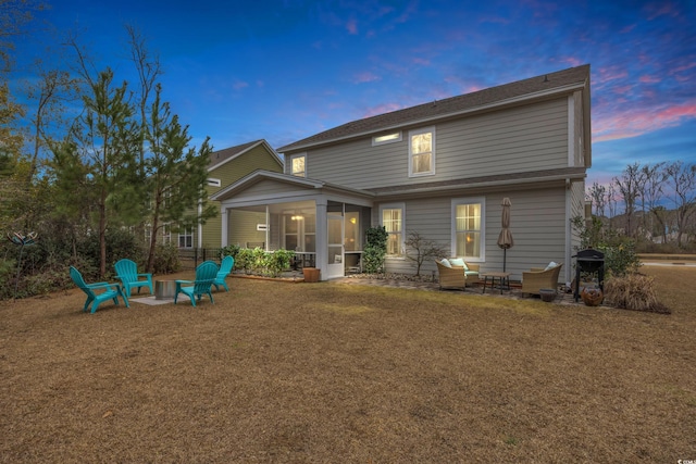 rear view of house featuring a lawn, a fire pit, a patio area, and a sunroom