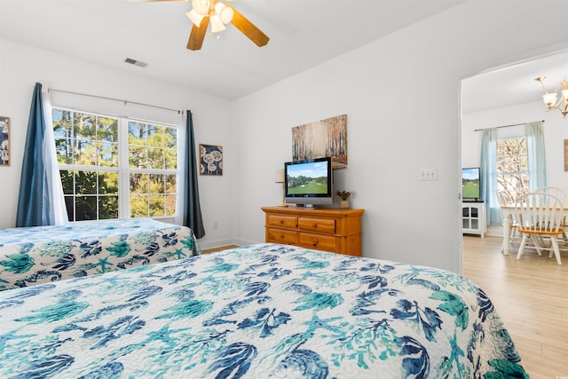 bedroom featuring ceiling fan with notable chandelier, multiple windows, and light hardwood / wood-style flooring