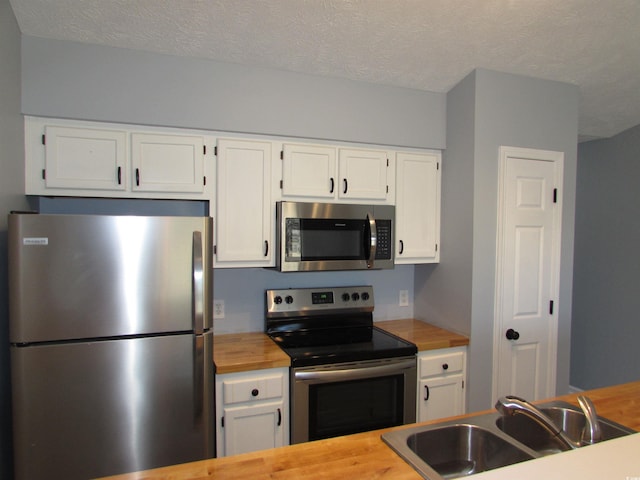 kitchen with appliances with stainless steel finishes, sink, white cabinets, and a textured ceiling