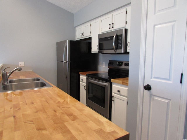 kitchen featuring white cabinetry, sink, butcher block countertops, and appliances with stainless steel finishes