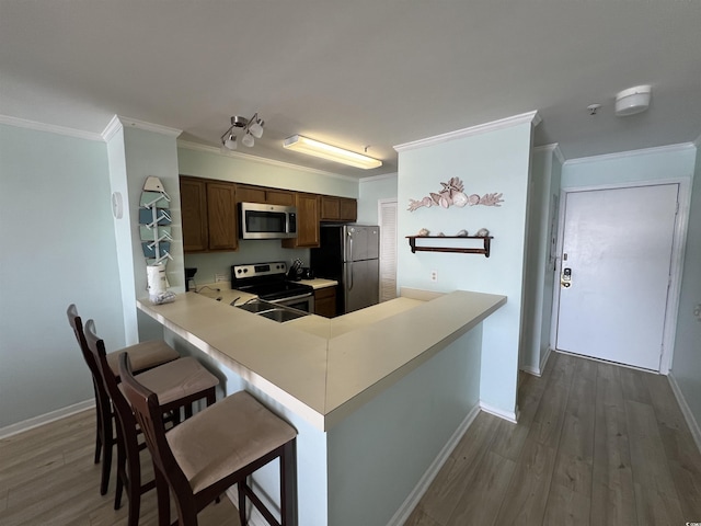 kitchen with stainless steel appliances, hardwood / wood-style flooring, kitchen peninsula, a breakfast bar area, and crown molding