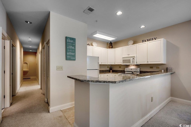 kitchen featuring white appliances, dark stone counters, kitchen peninsula, and white cabinets