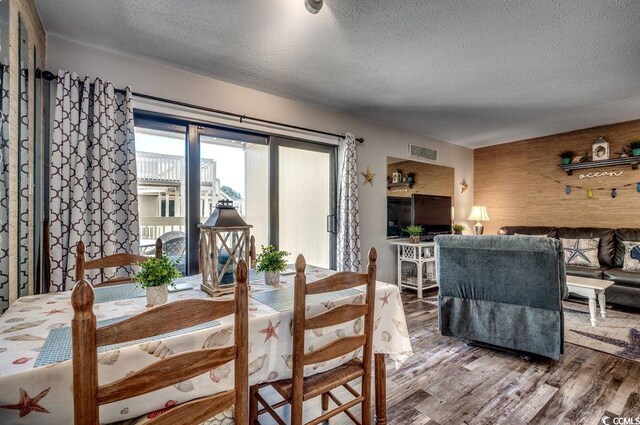 dining room featuring wood-type flooring, wood walls, and a textured ceiling