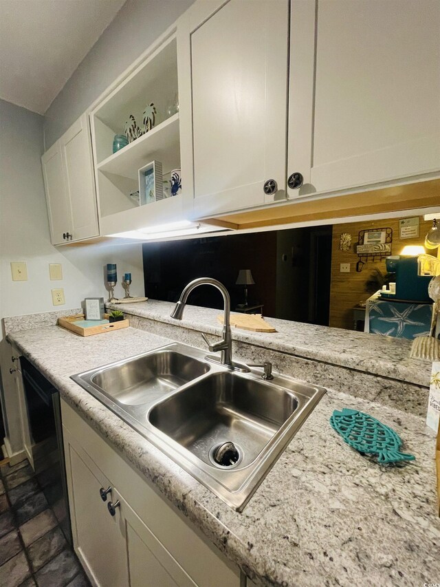 kitchen with light stone countertops, white cabinetry, dishwasher, and sink