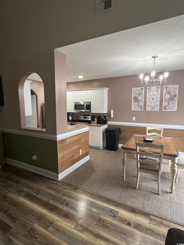 389 Cabo Loop, Myrtle Beach, SC 29588 - kitchen with appliances with stainless steel finishes, white cabinets, wood finished floors, a chandelier, and arched walkways