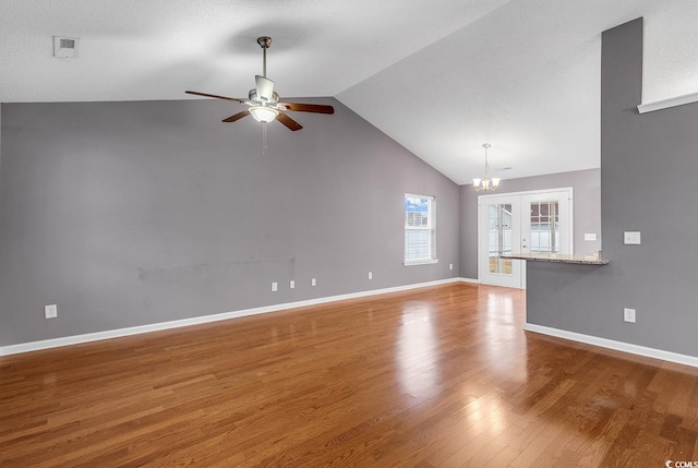 unfurnished living room with ceiling fan with notable chandelier, hardwood / wood-style floors, and vaulted ceiling