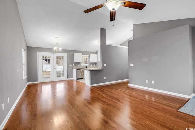 unfurnished living room with sink, vaulted ceiling, french doors, light hardwood / wood-style floors, and ceiling fan with notable chandelier