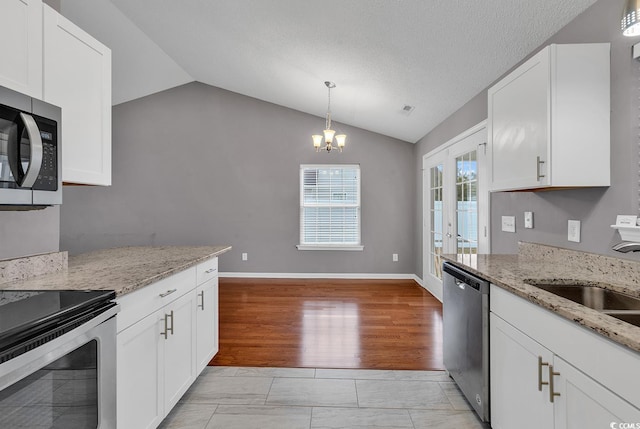 kitchen with vaulted ceiling, hanging light fixtures, stainless steel appliances, white cabinetry, and sink