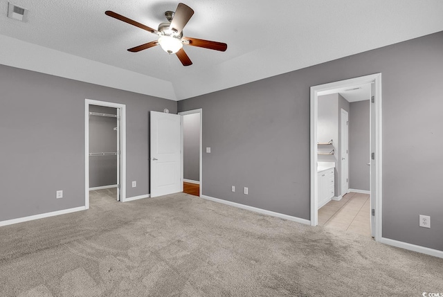 unfurnished bedroom with ensuite bath, ceiling fan, a spacious closet, and light carpet