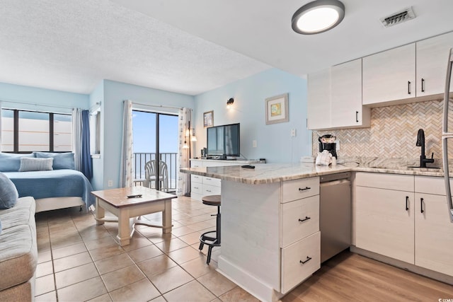 kitchen featuring stainless steel dishwasher, kitchen peninsula, light stone counters, and sink