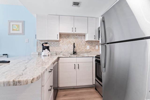 kitchen with light hardwood / wood-style floors, kitchen peninsula, appliances with stainless steel finishes, backsplash, and sink