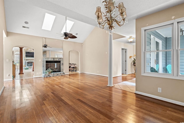 unfurnished living room featuring ceiling fan, a wealth of natural light, a stone fireplace, and hardwood / wood-style flooring