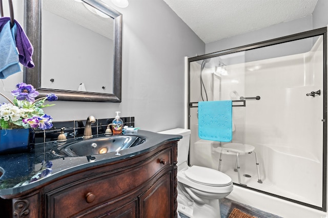 bathroom featuring a textured ceiling, toilet, walk in shower, and vanity