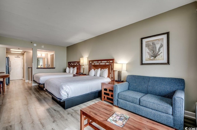 bedroom featuring light wood-type flooring, freestanding refrigerator, and baseboards