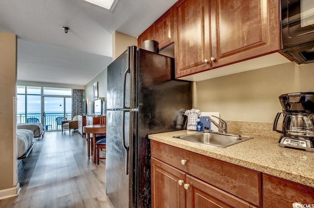 kitchen featuring brown cabinets, black appliances, light wood-style floors, and a sink