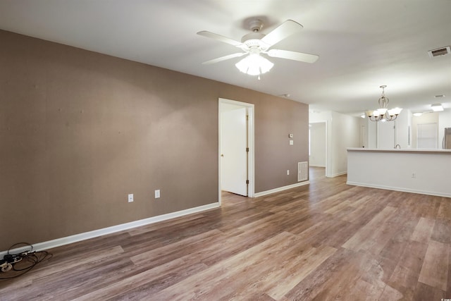 unfurnished living room with ceiling fan with notable chandelier and light hardwood / wood-style floors