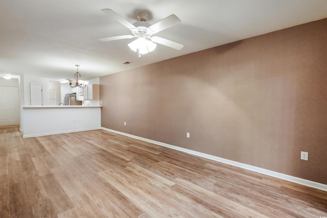 unfurnished living room featuring ceiling fan with notable chandelier and light hardwood / wood-style flooring