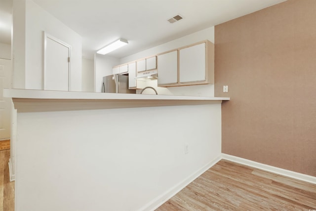 kitchen with kitchen peninsula, white cabinets, stainless steel refrigerator, light hardwood / wood-style flooring, and sink