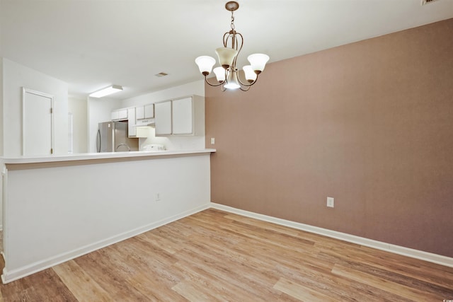 kitchen with decorative light fixtures, white cabinetry, stainless steel fridge, kitchen peninsula, and a notable chandelier