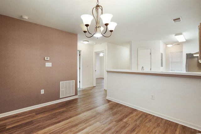 empty room with wood-type flooring and a notable chandelier