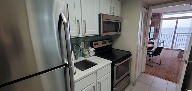 kitchen featuring sink, white cabinets, tasteful backsplash, light tile patterned floors, and appliances with stainless steel finishes