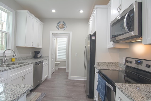 kitchen with appliances with stainless steel finishes, light stone countertops, dark wood-type flooring, white cabinets, and sink