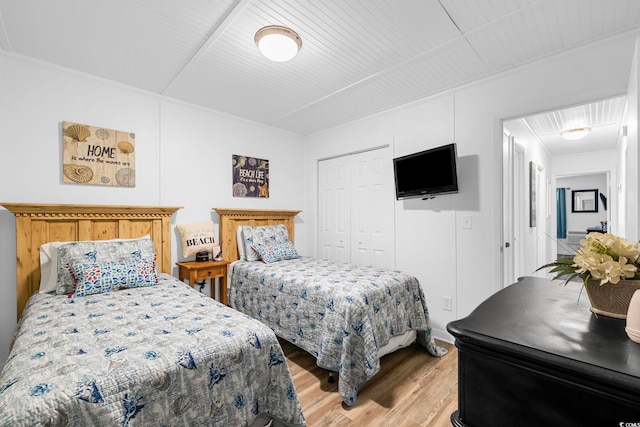 bedroom featuring light wood-type flooring, ornamental molding, and a closet