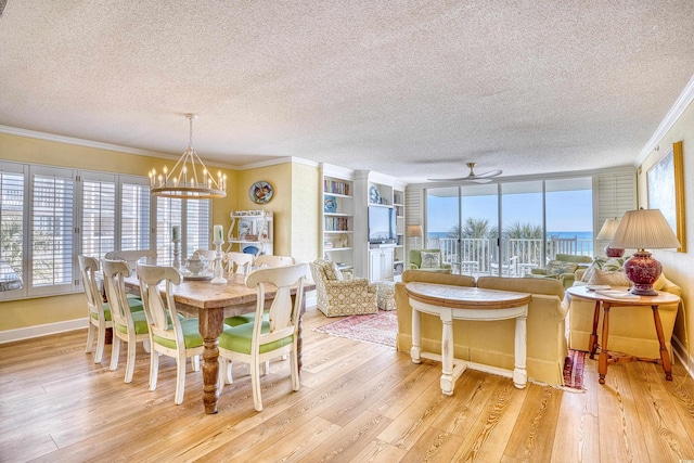 dining room featuring a textured ceiling, light wood-type flooring, crown molding, and ceiling fan with notable chandelier