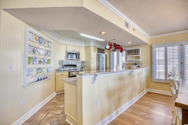 kitchen with a breakfast bar area, appliances with stainless steel finishes, kitchen peninsula, light stone counters, and a textured ceiling