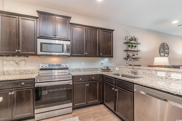 kitchen featuring sink, stainless steel appliances, dark brown cabinetry, light stone countertops, and light wood-type flooring