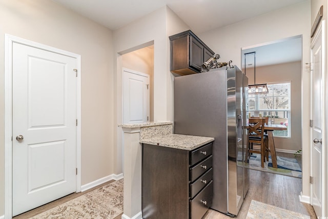 kitchen featuring light stone countertops, dark brown cabinets, stainless steel fridge, and light hardwood / wood-style flooring