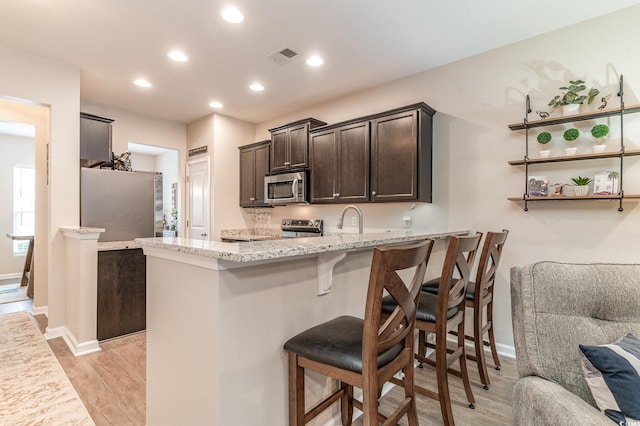 kitchen with a breakfast bar, light hardwood / wood-style flooring, appliances with stainless steel finishes, kitchen peninsula, and light stone countertops