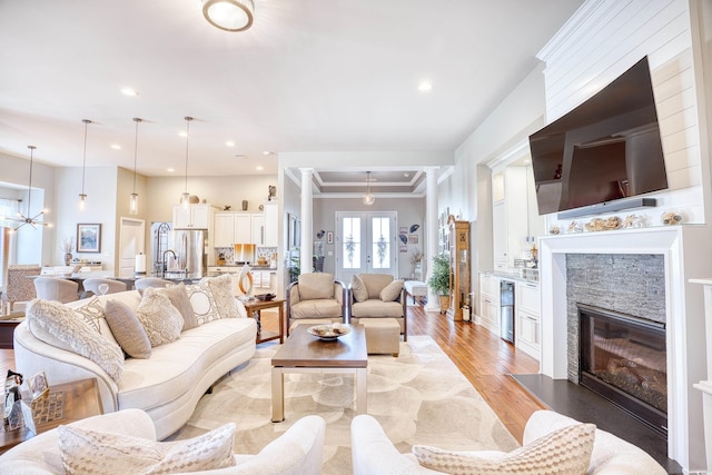 living room with a chandelier, ornamental molding, light hardwood / wood-style flooring, and a stone fireplace