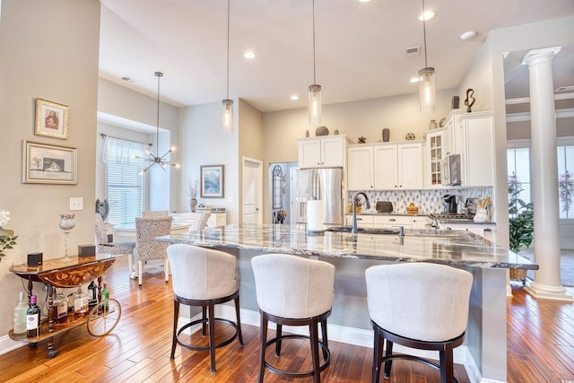 kitchen with a breakfast bar, stainless steel refrigerator with ice dispenser, decorative light fixtures, backsplash, and decorative columns