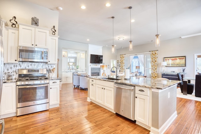 kitchen featuring stainless steel appliances, sink, an island with sink, decorative backsplash, and pendant lighting