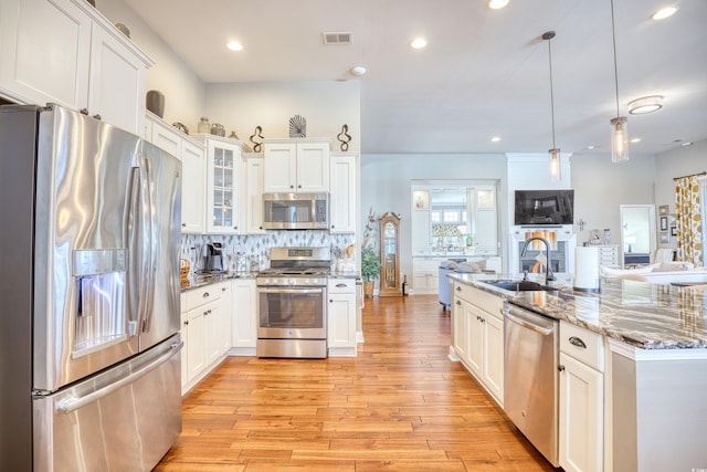 kitchen with white cabinets, light wood-type flooring, decorative backsplash, pendant lighting, and appliances with stainless steel finishes